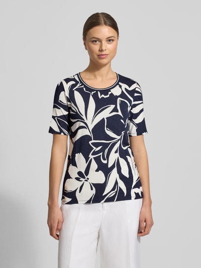 Frauenmodel trägt T-Shirt aus Viskose-Elasthan-Mix im Allover-Look von Betty Barclay, Damen T-Shirt, Regular-Fit, Rundhalsausschnitt, Rückenlänge 52 cm, Größe 36, marineweiß mit großflächigem Blumenmuster, feine und glatte Textur, Ganzkörperansicht von vorne.