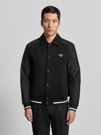 Männermodel trägt schwarze Jacke mit Label-Detail von Antony Morato, Kentkragen, Druckknopfleiste, Regular Fit, Nahaufnahme Oberkörper.