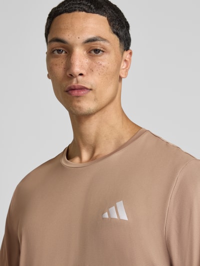 Männermodel trägt męski t-shirt Regular Fit Sport-T-Shirt mit Logo-Print Modell 'Run Ess Tee M' von adidas Training, beżowy kolor, gładka faktura, Nahaufnahme Oberkörper