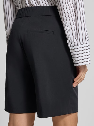 Frauenmodel trägt Schlupfbermuda Techno Cotton Superstretch von Raffaello Rossi, Regular-Fit, Modell ISKA, Gesäßtaschen, Elastikbund, Farbe Schwarz, glatte Oberfläche, Kontext: Damen Schlupfbermuda, Bundweite 39 cm, Innenbeinlänge 24 cm, Ganzkörperansicht Rückansicht.