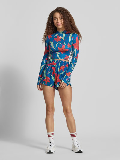 Frauenmodel trägt Slim Fit Sport-Langarmshirt mit Allover-Muster von adidas Sportswear, floral, Kontraststreifen, hochgeschlossen, AEROREADY, Interlock, Ganzkörperansicht von vorne.