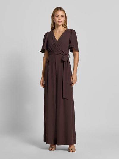 Frauenmodel trägt Jumpsuit mit Stoffgürtel von Rinascimento in Dunkelbraun, V-Ausschnitt, tailliert, glatte Textur, Ganzkörperansicht von vorne. Material-Mix mit Stretch-Anteil, kurzes Ärmel-Design, Raffungen.
