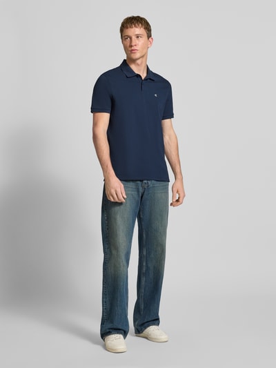 Männermodel trägt Straight Fit Poloshirt mit Label-Stitching von Calvin Klein Jeans in Dunkelblau, reine Baumwolle, Ganzkörperansicht von vorne.