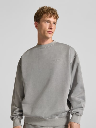 Männermodel trägt Relaxed Fit Sweatshirt aus Baumwoll-Mix von PEGADOR in Grau mit Logo-Stickerei, überschnittenen Schultern, Nahaufnahme Oberkörper.
