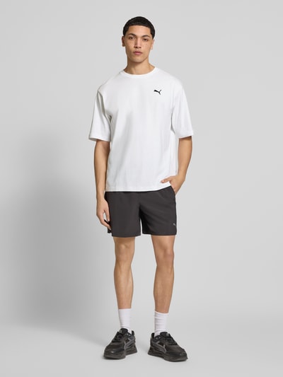 Männermodel trägt Herren T-Shirt mit Rundhalsausschnitt von PUMA PERFORMANCE aus Reine Baumwolle, Relaxed-Fit, weiß mit Logo, Ganzkörperansicht von vorne.