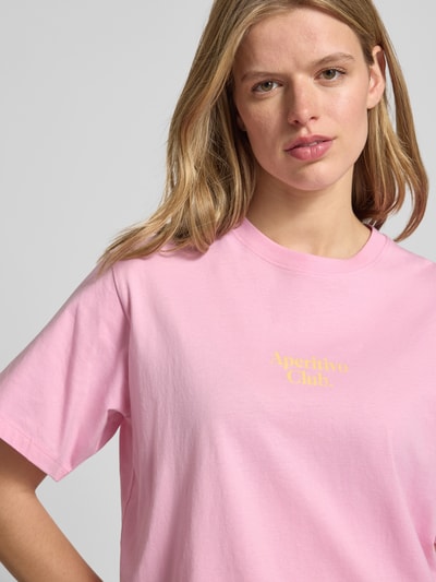 Frauenmodel trägt T-Shirt mit Statement-Print Modell 'SENNA' von JJXX in Rosa, reine Baumwolle, gerippter Rundhalsausschnitt, Nahaufnahme Oberkörper.