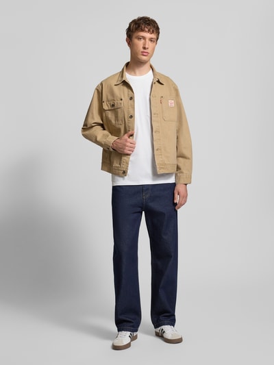 Męski model nosi Jeans mit Eingrifftaschen Modell 'Landon Pant Robertson' od Carhartt Work In Progress, bawełna, krój relaxed fit, szerokość w rozmiarze 32: 44 cm, długość nogawki wewnętrznej 78 cm, granatowy, gładka faktura, widok całej sylwetki z przodu.