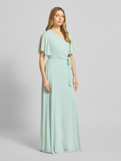 Vrouwenmodel draagt Regular Fit avondjurk met V-hals van Christian Berg Cocktail in mintgroen, taillering, korte mouwen, stofriem, lichte, vloeiende stof, voering, wrap-look, vooraanzicht hele lichaam.