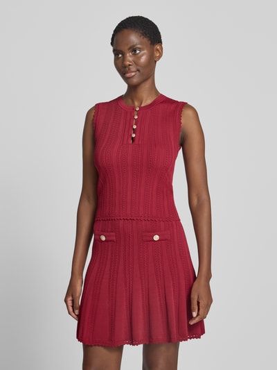 Frauenmodel trägt Stricktop in Pointelle-Strick mit kurzer Knopfleiste von GUESS, körpernaher Schnitt, Rundhalsausschnitt, Rot, Nahaufnahme Oberkörper.