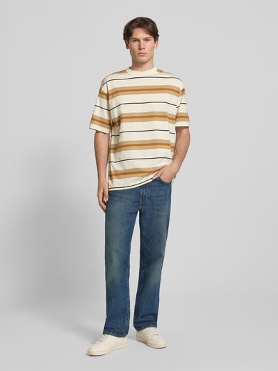Mannermodel draagt Oversized Shirt aus reiner Baumwolle Modell 'NIVARSI' van HUGO in brede beige en bruin gestreepte kleuren, heren oversized fit context, geheellichaamsvoorzijde.