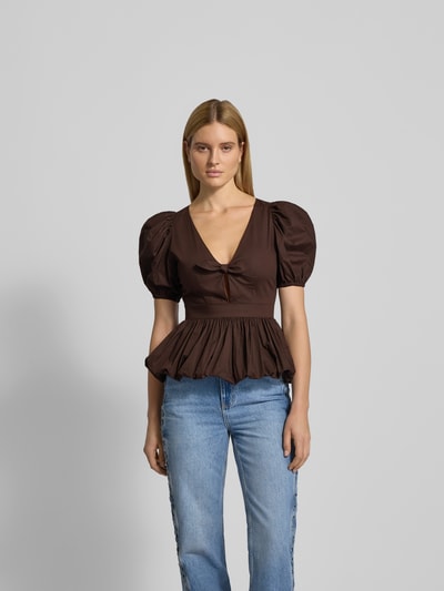 Frauenmodel trägt Blusenshirt mit V-Ausschnitt von ROTATE in Braun, Reine Baumwolle, Lockerer-Schnitt, Schleifen-Detail, Ganzkörperansicht von vorne.