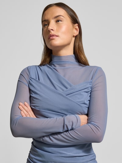 Frauenmodel trägt Slim Fit Langarmshirt aus semitransparentem Mesh Modell 'C_ETULAH' von BOSS Orange, Optik: Unifarben, Wickeloptik, hochgeschlossen, langarm, offene Kanten, Mesh-Materialverarbeitung, Ganzkörperansicht von vorne.