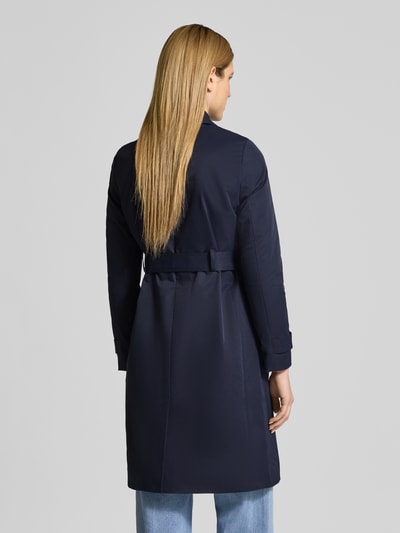 Frauenmodel trägt dunkelblauen Trenchcoat mit Ärmelriegeln von Christian Berg Woman Selection, taillierte Passform, Ganzkörperansicht Rückansicht.
