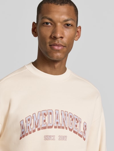 Männermodel trägt Relaxed Fit Sweatshirt aus reiner Baumwolle Modell 'WORDMARK' von ARMEDANGELS in Beige mit Aufdruck, Nahaufnahme Oberkörper. Herren Sweatshirt von ARMEDANGELS.