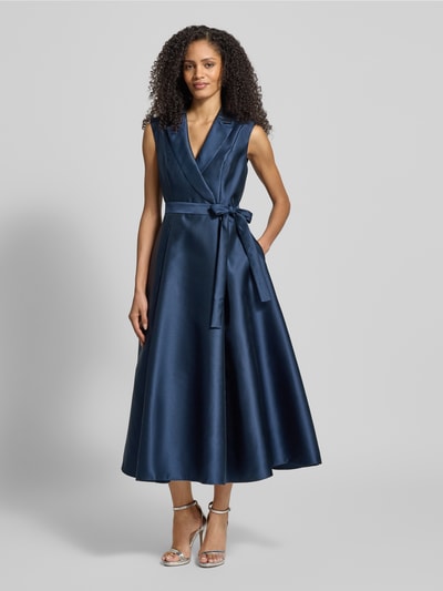 Frauenmodel trägt Cocktailkleid mit Reverskragen von Adrianna Papell, Taillierter Schnitt, Taillengürtel, blickdichtes Unterkleid, Nahtreißverschluss, glänzender dunkelblauer Stoff, Ganzkörperansicht von vorne.
