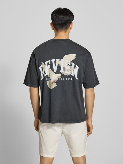 Männermodel trägt T-Shirt mit Logo- und Motiv-Print von REVIEW in Schwarz, Reine Baumwolle, Loose-Fit, Ganzkörperansicht Rückansicht.