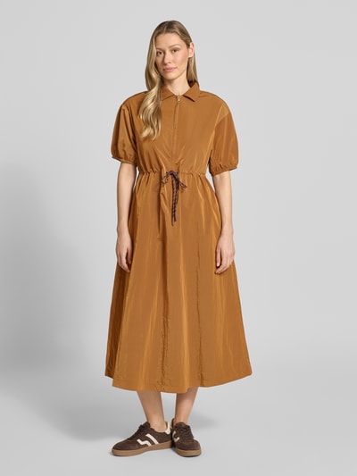 Frauenmodel trägt Midikleid mit kurzem Reißverschluss und Kordelzug an der Taille von Rich & Royal in Braun, glänzende Textur, Ganzkörperansicht von vorne. Taillierter Schnitt, gerippter Kentkragen, 1/2-Arm mit elastischen Abschlüssen, mittellange Länge.