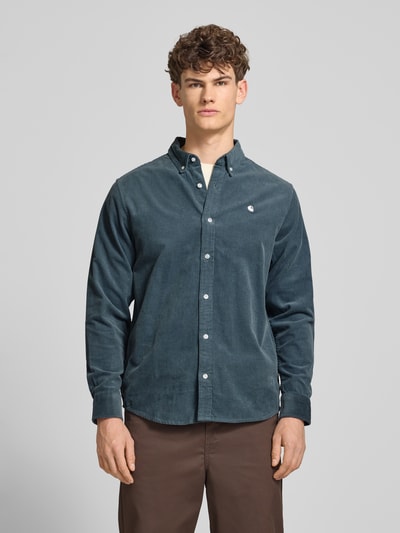 Męski model nosi Regular Fit Freizeithemd aus Cord mit Button-Down-Kragen od Carhartt Work In Progress, bawełna, model Madison, szerokość w rozmiarze M 44 cm, długość tyłu 76 cm, długość rękawa 64 cm, faktura sztruksowa, kolor ciemnoniebieski, naszyte logo, widok całej sylwetki z przodu