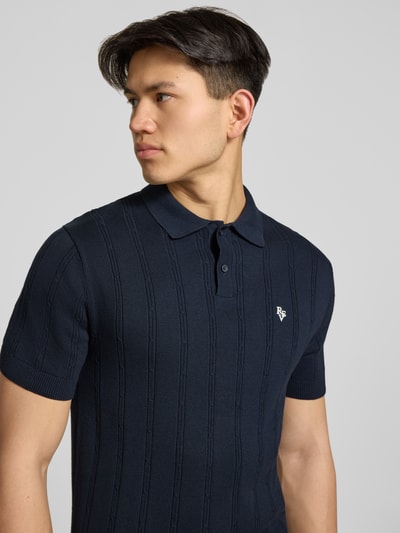 Männermodel trägt Slim Fit Strick-Poloshirt mit Label-Stitching von REVIEW in Dunkelblau, Zopfmuster, Nahaufnahme Oberkörper.