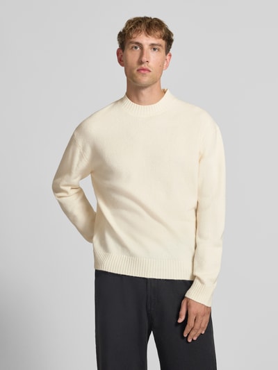 Männermodel trägt Relaxed Fit Strickpullover aus Material-Mix mit Baumwoll-Anteil von REVIEW in Creme, strukturierte Optik, Ganzkörperansicht von vorne. Rückenlänge 66 cm, Ärmellänge 61 cm, Stehkragen, elastische Abschlüsse.