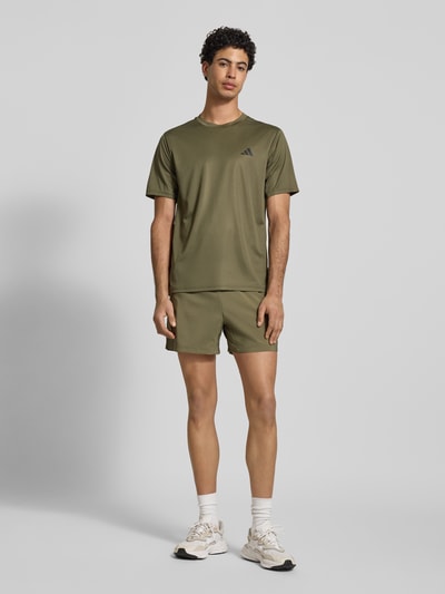 Männermodel trägt Shorts mit elastischem Bund von adidas Training in Olivgrün, mit Reißverschlusstaschen, Label-Print, Lockerer-Schnitt, Ganzkörperansicht von vorne.