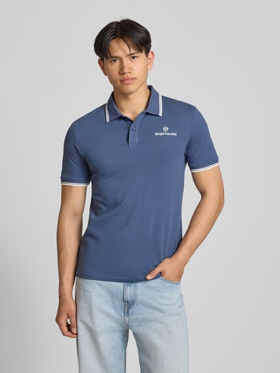 Männermodel trägt Slim Fit Poloshirt mit Logo-Stitching Modell 'Reed' von SERGIO TACCHINI in Blau, elastischer Baumwoll-Mix, Kurzarm, Polokragen, Ganzkörperansicht von vorne.