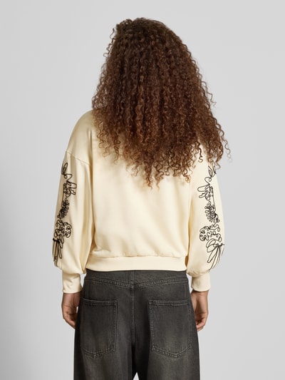 Männermodel trägt Relaxed Fit Sweatshirt aus mieszanka bawełny model 'BROOKE' von ONLY, kremowa bluza z czarnym haftem na rękawach, Ganzkörperansicht Rückansicht, Damen bluza od ONLY