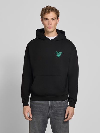 Männermodel trägt Relaxed Fit Hoodie mit Motiv-Print von REVIEW x ANSON´S, schwarz, Baumwoll-Mix, gerippte Abschlüsse, Langarm, Ganzkörperansicht von vorne.
