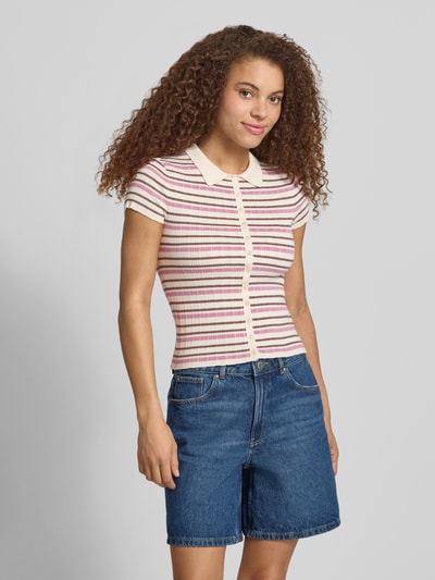 Modelka nosi Slim Fit Strick-Poloshirt aus Viskose-Mix von Review w paski, różowy i kremowy, zapięcie na guziki, krój slim fit, widok z przodu, ujęcie całej sylwetki.