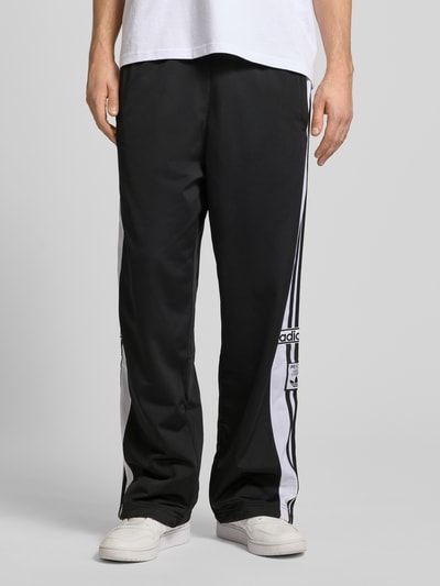Männermodel trägt Trainingshose mit Label-Details und elastischem Bund von adidas Originals, Relaxed Fit, Schwarz-Weiß, Ganzkörperansicht von vorne. Modell 'ADIBREAK', Innenbeinlänge bei Größe M: 75 cm.