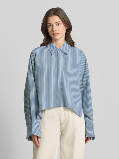 Männermodel trägt Relaxed Fit Bluse aus Viskose-Mix Modell 'OSHIA' von Drykorn, niebieski w białe paski, kołnierz koszulowy, z ukrytym zapięciem, długość tyłu 59 cm, długość rękawa 65 cm, Ganzkörperansicht von vorne.
