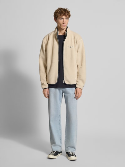 Männermodel trägt Teddyjacke mit Reißverschluss von Pegador in Beige mit Stehkragen, Regular Fit, Label-Stitching, Ganzkörperansicht von vorne.