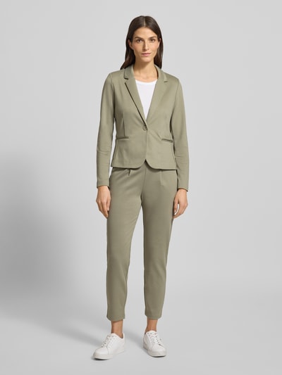 Frauenmodel trägt Slim Fit Stoffhose mit Viskose-Anteil Modell 'Rizet' von B.Young in hellem Oliv, 7/8-Länge, Ganzkörperansicht von vorne. Elastischer Bund mit Tunnelzug und Bundfalten, glatte Textur, passend zum Kontext Damen Stoffhose, bequemer Material-Mix.