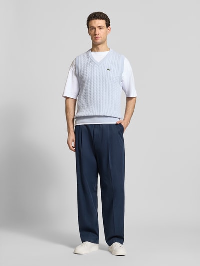 Männermodel trägt Regular Fit Pullunder aus Baumwoll-Mix von Lacoste in Hellblau mit Zopfmuster, unifarben, Strickoptik, Logo-Detail, Ganzkörperansicht von vorne.