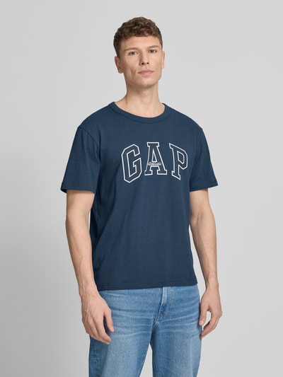 Männermodel trägt T-Shirt mit Logo und Rundhalsausschnitt von GAP in Dunkelblau, Reine Baumwolle, Regular-Fit, Ganzkörperansicht von vorne.