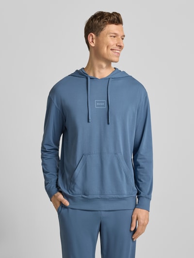 Männermodel trägt Regular Fit Hoodie aus Baumwoll-Mix Modell 'LAZE' van HUGO in effen blauw met labelprint, kangoeroezak, zweetstof, Ganzkörperansicht von vorne.