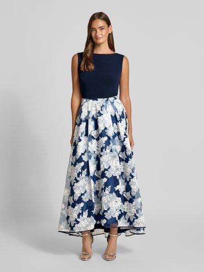 Vrouwenmodel draagt avondjurk met rugdecolleté van Christian Berg Cocktail, materiaalmix met viscose, getailleerd model, midi-jurk, boothals, zoom, voor kort en achter lang, kleur donkerblauw met witte bloemen, ruglengte maat 36: 131 cm, borstwijdte 43 cm. Ganzkörperansicht von vorne.