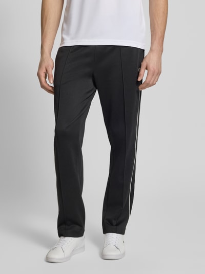 Männermodel trägt Regular Fit Sweatpants mit Baumwoll-Anteil von Lacoste in Schwarz mit weißen Galonstreifen, Logo-Applikation, seitliche Eingrifftaschen, Sweat-Material-Mix; Ganzkörperansicht von vorne.