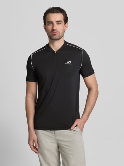 Männermodel trägt Regular Fit T-Shirt mit Stehkragen von EA7 Emporio Armani in Schwarz mit Reißverschluss und Label-Print, Ganzkörperansicht von vorne.