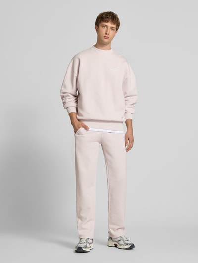Männermodel trägt Oversized Sweatshirt mit Label-Stitching von Pegador in hellem Rosa, Baumwoll-Mix, Rundhalsausschnitt, Ganzkörperansicht von vorne.