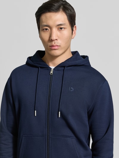 Männermodel trägt Regular Fit Sweatjacke aus Baumwoll-Mix von Tom Tailor Denim in Dunkelblau, Kapuze mit Tunnelzug, Logo-Detail, Nahaufnahme Oberkörper