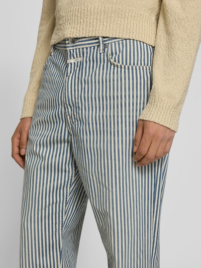 Männermodel trägt Straight Fit Jeans mit Logo-Patch von Closed aus Reine Baumwolle, blauer Streifenprint, Nahaufnahme Oberkörper. Innenbeinlänge 80 cm, Bundweite 42 cm, Eingriff- und Gesäßtaschen, Knopf- und Reißverschluss.