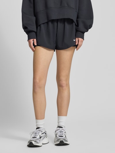 Frauenmodel trägt schwarze Shorts im 2-in-1-Look mit Logo Modell 'One' von NIKE TRAINING, Regular-Fit, elastischer Bund; Ganzkörperansicht von vorne. Damen Shorts, Bundweite bei Größe S 35 cm, Innenbeinlänge 8 cm.