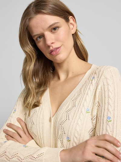 Modelka kobieca nosi Regular Fit Strickjacke aus Baumwoll-Mix model 'BIRTIE' od Only, efekt: jednolity kolor, faktura, ścieg warkoczowy, kwiatowe hafty, głęboki dekolt w serek, długie rękawy, prążkowane zakończenia, dzianina, mieszanka bawełny; zbliżenie na górną część ciała od przodu.