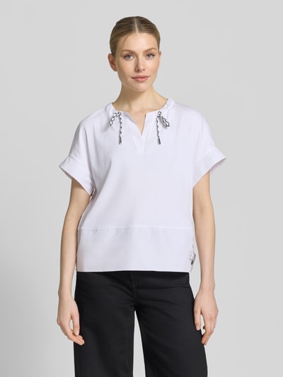 Modelka nosi T-Shirt mit Tunikakragen und Kordelzug od Marc Cain, biały bawełniany mix z domieszką stretchu, prosty krój, detale z logo, długość tyłu 55 cm w rozmiarze 36, widok całej sylwetki z przodu.