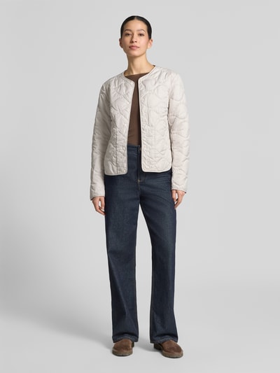 Vrouwenmodel draagt 'Steppjacke mit Rundhalsausschnitt' van camel active in beige met doorlopende drukknopen, rechte fit, quiltstiksels, ronde hals, schouderbreedte 43 cm, borstwijdte 53 cm, mouwlengte 64 cm, ruglengte 60 cm, voorkant volledig zichtbaar, Ganzkörperansicht von vorne.
