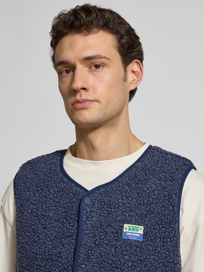 Männermodel trägt Straight Fit Weste mit Logo-Patch Modell 'Hoktown' von American Vintage aus dunkelblauem Kunstfell, Nahaufnahme Oberkörper.