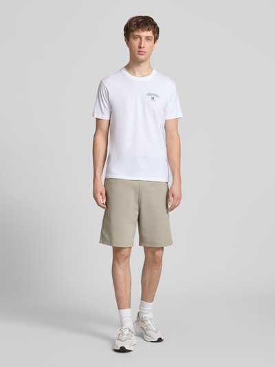Męski model nosi Shorts mit Label-Stitching mit elastischem Bund von CHAMPION, bawełniana mieszanka, krój regular fit, szerokość w rozmiarze M: 37 cm, długość nogawki wewnętrznej w rozmiarze M: 42 cm, jasnobeżowy kolor, całkowity widok z przodu.