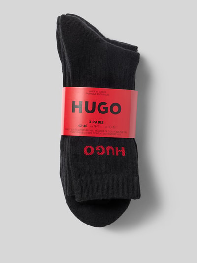 Productfoto, zwarte sokken van HUGO, effen design met rood HUGO-logo, zachte textuur, verpakt per drie paar