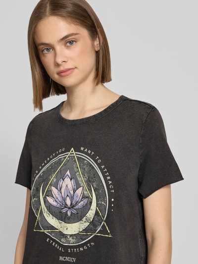 Frauenmodel trägt Leicht ausgestelltes Freizeitkleid aus reiner Baumwolle Modell 'LUCY' von Only, Dunkelgrau, Lotus-Motiv mit Glitzerprint, Jerseystruktur, Nahaufnahme Oberkörper.